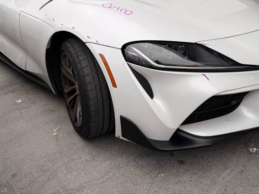 Before repair: white Toyota Supra front driver-side corner with scuffs on the bumper and fender