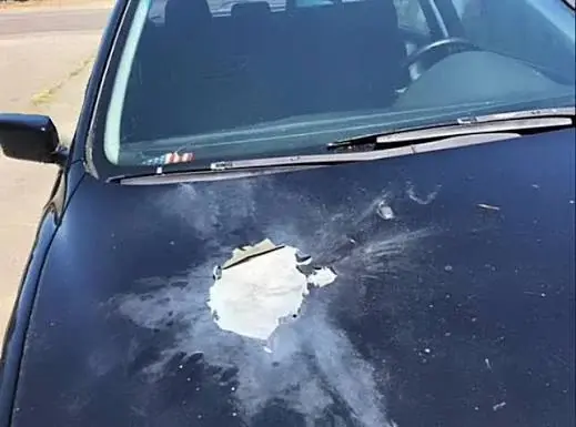 Black vehicle hood with a large firework blast mark and ash residue